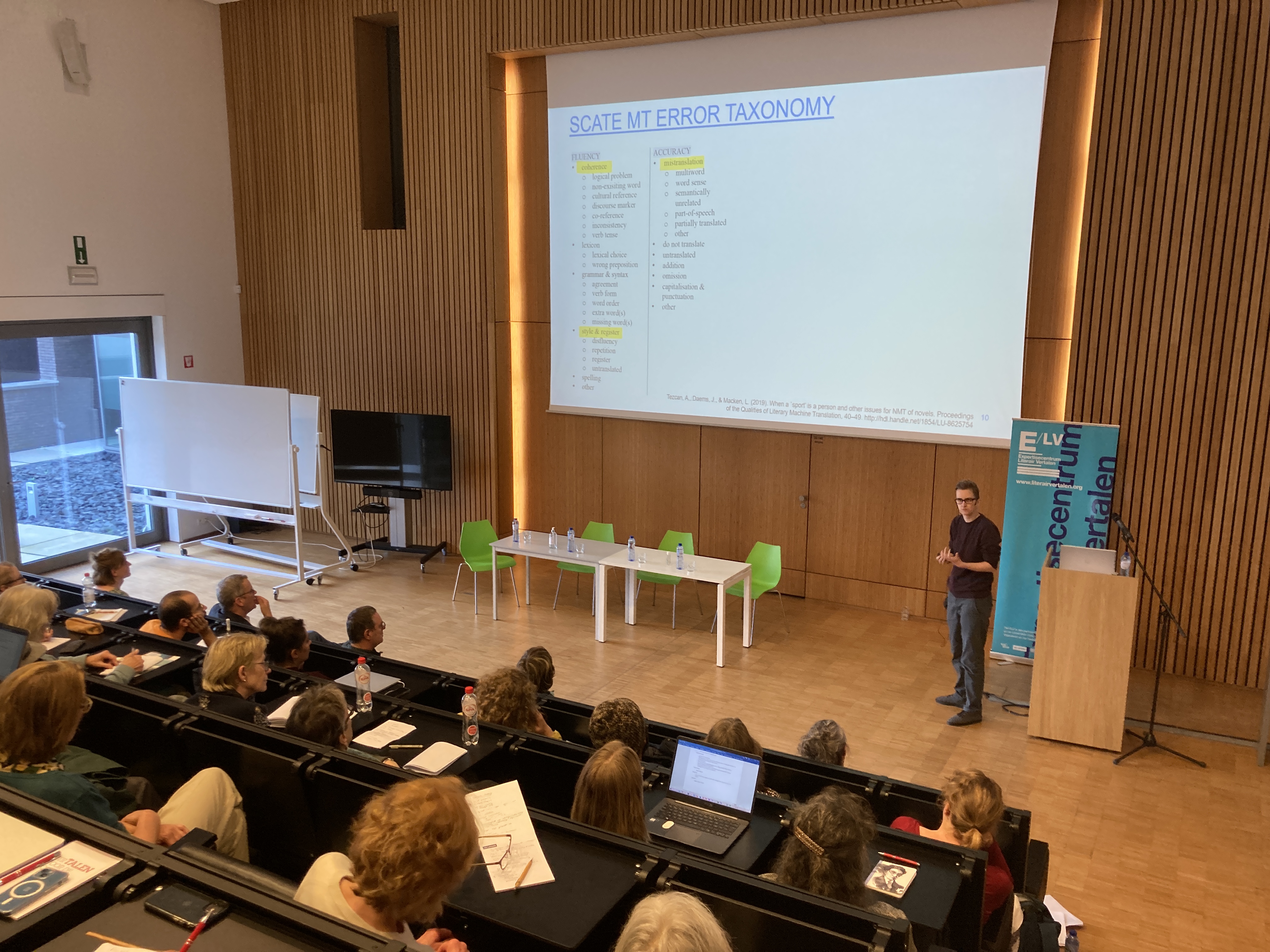 Foto van Joke Daems op het podium tijdens de studiemiddag, vanuit het publiek gezien.