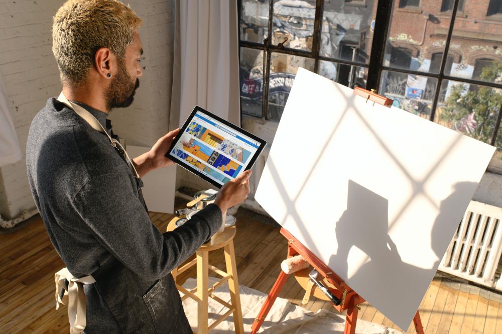 Foto van een persoon met een tablet in de hand voor een schildersezel bij het artikel De invloed van technologie op creativiteit in vertaling
