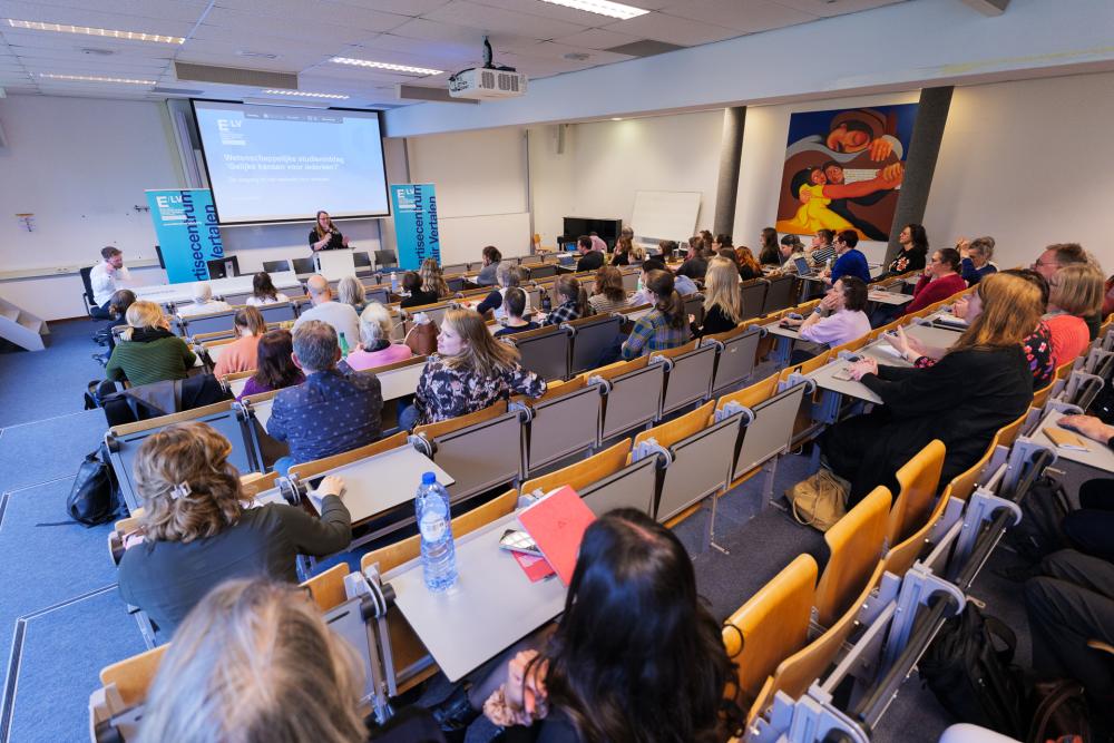 Foto van collegezaal gevuld met bezoekers die luisteren naar een spreker