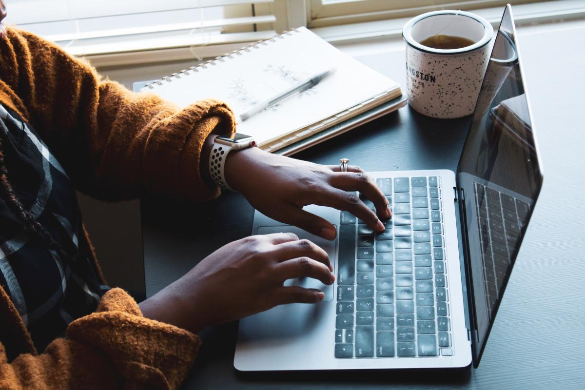 Decoratieve afbeelding van iemand die achter een laptop werkt met een kop koffie en een schrift.