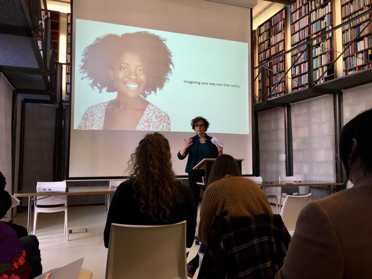 Nicolette Hoekmeijer geeft een lezing met op het diascherm een foto van een auteur met de tekst: 'Imagining our way into that reality'