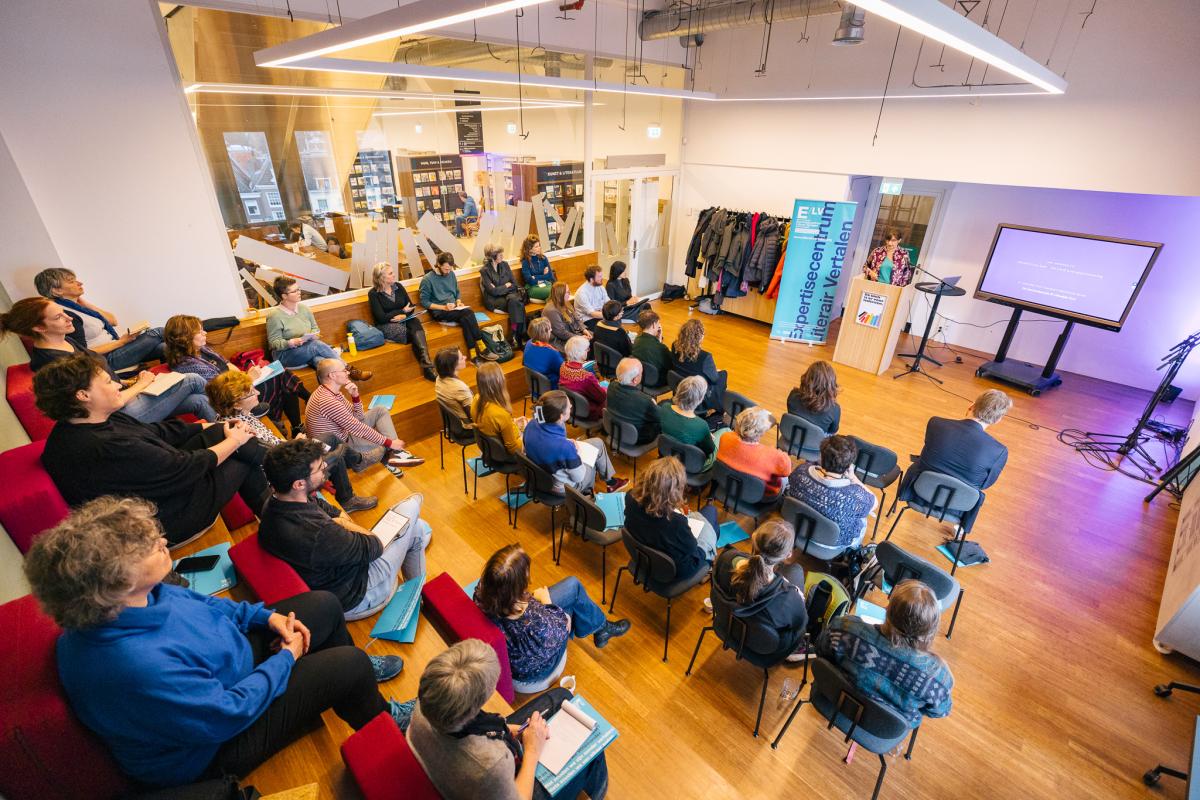 overzichtsfoto van een zaal met zittend publiek luisterend naar een spreker